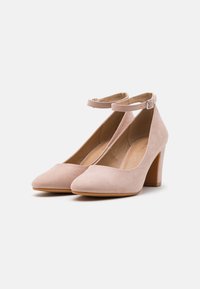 Scarpe con tacco alto in suede rosa, con cinturino alla caviglia, punta affusolata e tacco spesso. Design minimalista con una superficie liscia e un colore neutro.