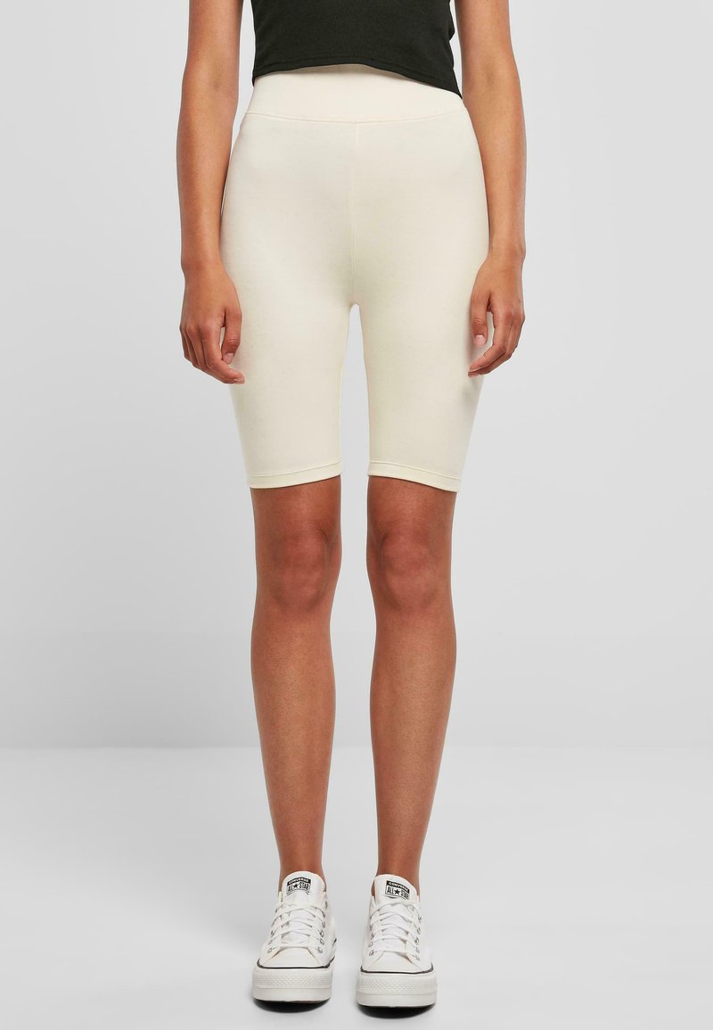 Des shorts de vélo couleur crème avec une taille haute, un tissu extensible et une texture lisse, associés à des baskets blanches basses.