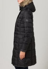 Zwarte pufferjas met een met bont gevoerde capuchon, gewatteerd ontwerp, zakken aan de voorkant en een logo-opdruk op de mouw. Glad textuur, medium lengte.