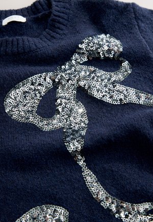 Pull bleu marine en tissu doux, orné d'un motif en sequins argentés ressemblant à un nœud, avec un col côtelé et une finition texturée.