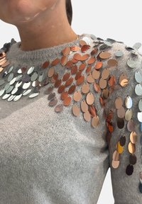 Maglione grigio a maglia con paillettes rotonde metalliche in rame e argento disposte diagonalmente sulle spalle, creando un effetto texturizzato.