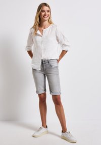 Chemise blanche en lin à boutons, short en denim gris retroussé et baskets blanches. La chemise a une coupe décontractée et un col rond.