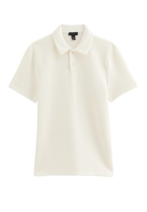 Polo in cotone a coste color crema a maniche corte con due bottoni e colletto classico, distesa su sfondo bianco.