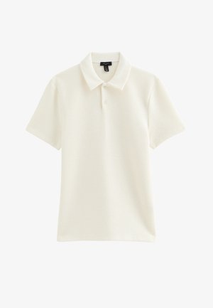 Kremowa koszulka polo z krótkim rękawem z prążkowanej bawełny, z dwoma guzikami i klasycznym kołnierzykiem, ułożona na płasko na białym tle.