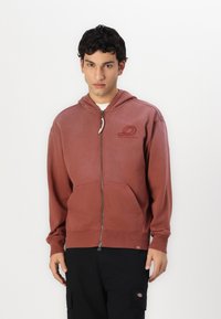 Bordo zip-up gobtuvė su priekinėmis kišenėmis, šonkauliniais rankogaliais ir apatine dalimi. Yra logotipas ant krūtinės ir raištelis ant gobtuvo. Pagaminta iš medvilnės mišinio.