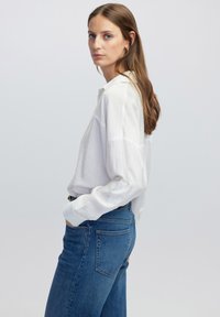 Witte lange mouwen blouse met een relaxte pasvorm en puntige kraag, gecombineerd met hooggetailleerde blauwe denim jeans met achterzakken.