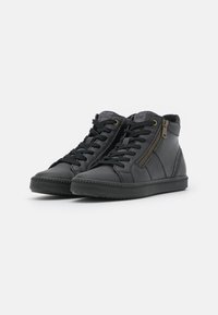 Paire de baskets montantes noires avec fermeture éclair latérale, lacets noirs et panneaux texturés sur fond blanc.