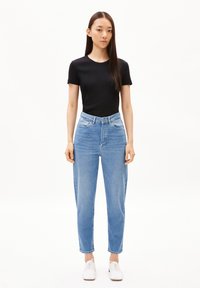 Top negro de mangas cortas combinado con jeans de tiro alto azules claros, con un corte relajado y una textura de denim clásica, completado con zapatos blancos.