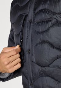 Marinblå pufferjacka med en texturerad, quiltad design, dragkedjeficka och tryckknappar. Tillverkad av lätt, vattenavvisande material.