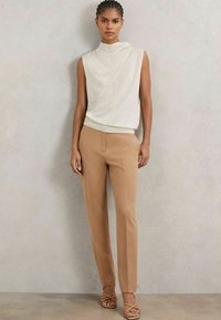 Kätev kreemjas ilmaääreta pluus pehme tekstuuriga, kokku sobitatud beezide ülikonnapükstega. Kammeljas sandaalid täiustavad komplekti.