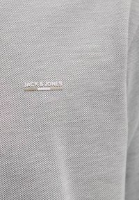 Tissu gris texturé avec un motif en maille, comportant une étiquette logo argentée "JACK & JONES". Accent sur le design et le détail du matériau ; simple et moderne.