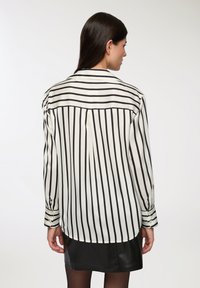 Blusa a maniche lunghe a righe bianche e nere con fit rilassato, polsini con bottoni e orlo arrotondato, realizzata in un tessuto leggero.