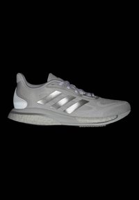 Grauer Sportschuh mit einem Mesh-Obermaterial, metallisch silbernen Streifen, strukturiertem Fersenbereich, reflektierenden Akzenten und einer gepolsterten weißen Außensohle.