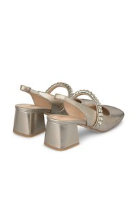 Talons en or métallique avec un bout pointu, un talon carré et une sangle décorative ornée de strass transparents sur le devant. Texture lisse.