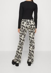 Svart långärmad topp kombinerad med figurnära byxor med ett svartvitt abstrakt mönster. Byxorna har utsvängt fåll och är tillverkade av texturerat tyg.