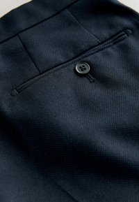 Marineblauwe textuurstof met een gladde afwerking, voorzien van een enkele zwarte knoop en een gestikte zakdetail.