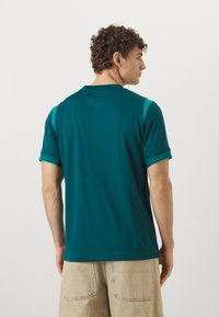 Teal short-sleeve polo shirt with a crew neck, featuring contrasting shoulder panels and subtle texture throughout the fabric.