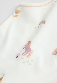 Witte stof met kleurrijke illustraties van een eenhoorn, bloemen, paddenstoelen en een regenboog. Zachte textuur met roze stiksels.