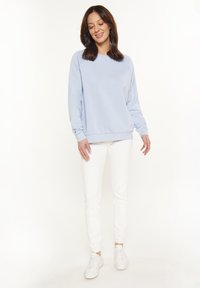 Felpa azzurro chiaro con polsini e orlo a costine, abbinata a pantaloni bianchi slim-fit e sneakers bianche. Tessuto liscio, vestibilità casual.