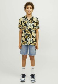 T-shirt kratkih rukava crne boje s uzorkom žutog voća i zelenog lišća, uparen s plavim trapericama i plavim tenisicama s bijelim detaljima.