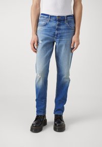 Bledé modré džíny z denimu s poškozenými detaily, rovný střih nohavic, design s pěti kapsami a zdobené kovovým zapínáním na knoflík.