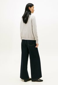 Grijze gebreide trui, losse donkere denim wijde pijpenbroek, zwarte schoenen. Gladde textuur en eenvoudig ontwerp, met zichtbare stikseldetails.