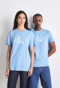 Gaiši zili kokvilnas T-krekli ar īsām piedurknēm, uz kuriem priekšpusē centrā ir balta logo "Calvin Klein Jeans". Standarta izmērs, minimālisma dizains.