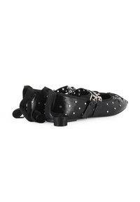 Bailarinas de cuero negro con punta redondeada, detalles de tachuelas, doble hebilla y correas alrededor del tobillo. Tacones bajos y gruesos que mejoran la estabilidad.