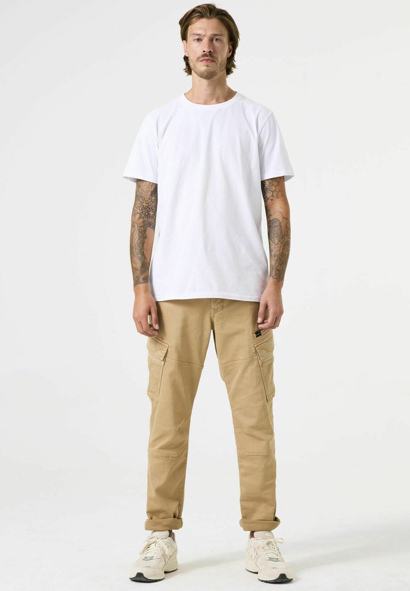 Witte katoenen t-shirt, relaxed fit, gecombineerd met beige cargo pants met zijzakken en omgeslagen mouwen. Schoeisel: lichte sneakers.