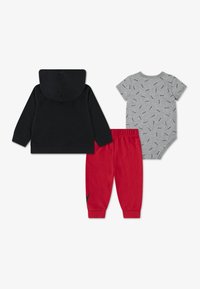 Komplet dječje odjeće u tri dijela: crna majica s kapuljačom, sivi bodi kratkih rukava s uzorkom i crvene hlače trenirka s crnim detaljima.