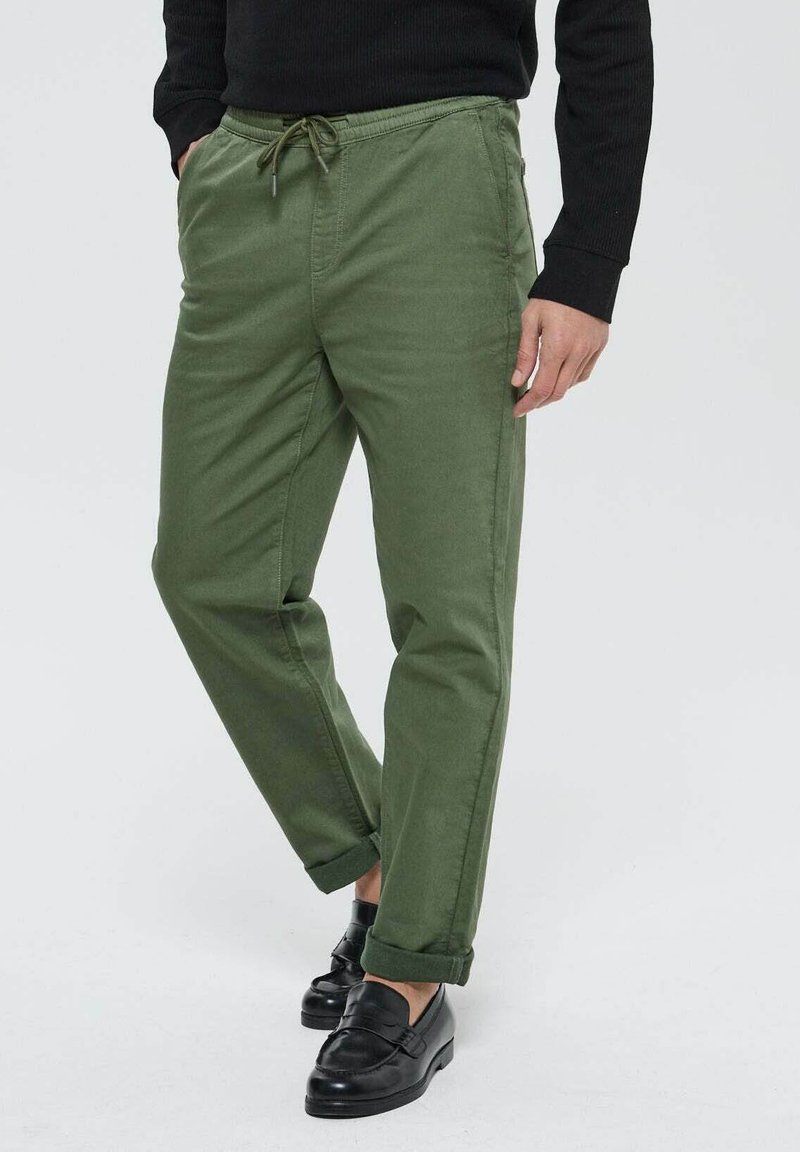 Pantalons en coton vert avec une taille élastique et un cordon de serrage, dotés de poches latérales et d'une coupe décontractée, associés à des mocassins noirs.