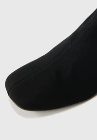 Μαύρο υφασμάτινο παπούτσι με μυτερή μύτη, λεία επιφάνεια και χωρίς ραφές. Διαθέτει ελαστική σόλα για άνεση και ευκολία στην κίνηση.