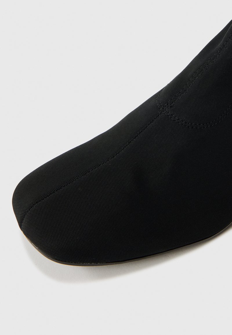 Schwarzer Textilschuh mit spitzer Zehenpartie, glatter Oberfläche und nahtlosem Design. Verfügt über eine flexible Sohle für Komfort und Bewegungsfreiheit.