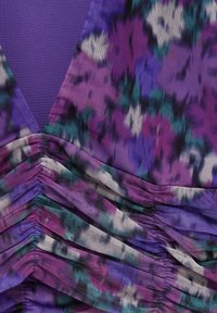 Gros plan d'un tissu violet froncé avec un imprimé floral abstrait en bleu sarcelle, noir et blanc et une texture en maille.