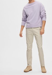 Sweatshirt en lavande texturé, pantalon slim beige et chaussures en daim beige clair, avec un col rond et des poignets flexibles.