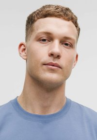 Hele sinise värvi dressipluus, millel on ribatud ümar kaelus, sile tekstuur ja minimaalne disain. Mudel näitab neutraalset ilmet.