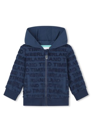 Veste à capuche zippée bleu marine avec un tissu texturé présentant un motif de logo répété, des poignets côtelés et des poches latérales.