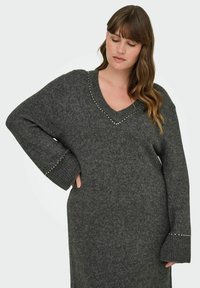 Kolgrå stickad klänning med v-ringning, prydd med silverfärgade nitar längs halslinningen och vida ärmar. Mjuk, texturerad tyg.