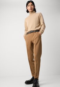 Bežna pulover s turtleneck ovratnikom iz mehkih materialov, v kombinaciji s svetlo rjavimi hlačami. Črni usnjeni pas in črni čevlji z debelim podplatom.