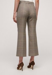 Rutig byxor med medelhög midja, kortade utställda ben och flerfärgat rutmönster. Materialet verkar ha en texturerad yta; tillsammans med bruna klackar.