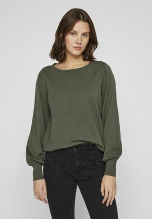 Maglione verde a maglia con scollatura rotonda, maniche lunghe a sbuffo e polsini a coste. Abbinato a pantaloni neri aderenti.