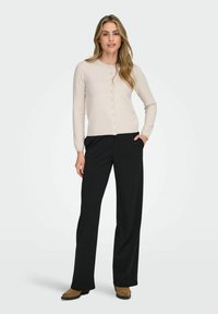 Lys beige cardigan med rund halsudskæring, knaplukning foran og lange ærmer, parret med sorte breddebenede bukser og brune ankelstøvler.