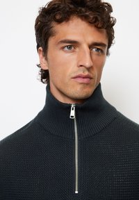 Dark knit sweater with a high collar, featuring a silver zipper, textured pattern, and a form-fitting design.