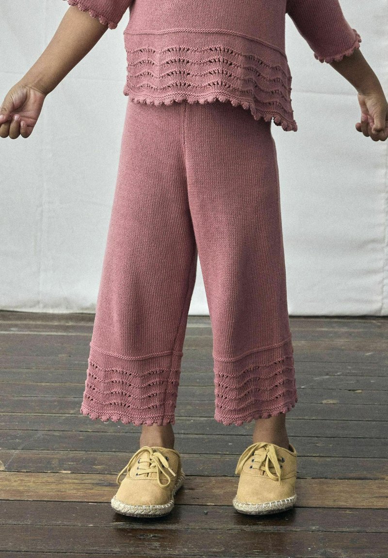 Roze gebreide outfit met cropped pants met een scalloped zoom en een bijpassend top. Zachte textuur; gecombineerd met beige espadrille schoenen.