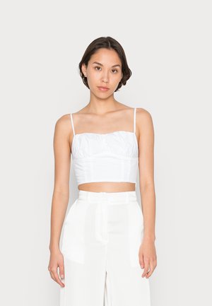 Top branco curto com alças finas, apresentando uma textura franzida na região do peito. Combinado com calças brancas de perna larga e cintura alta.