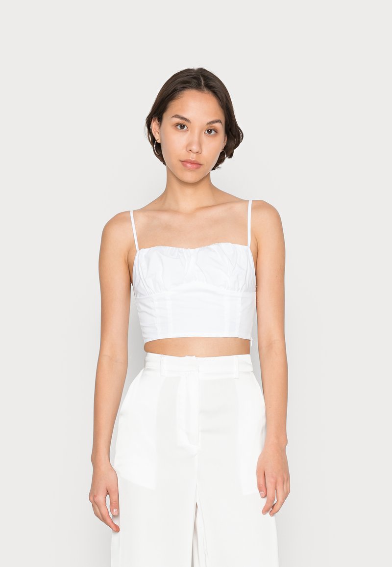 Top branco curto com alças finas, apresentando uma textura franzida na região do peito. Combinado com calças brancas de perna larga e cintura alta.