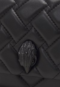 Czarna, pikowana skórzana powierzchnia z matowym, czarnym metalowym zapięciem w kształcie ptasiej szpony w centrum.