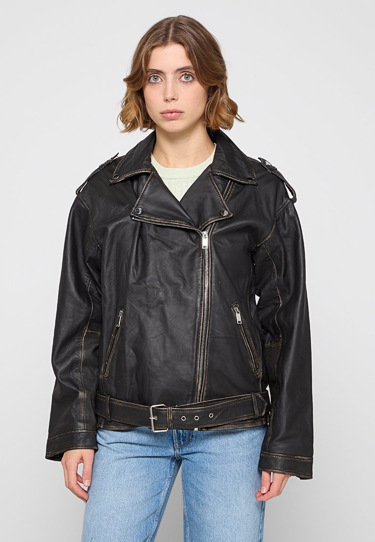 Czarna skórzana kurtka motocyklowa z wysokim kołnierzem, srebrnymi zamkami błyskawicznymi i akcentami paska; charakteryzuje się luźnym krojem i widocznym przeszyciem.