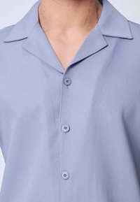 Gros plan sur une personne portant une chemise à boutons bleu clair avec un col, montrant le cou et la partie supérieure de la poitrine.