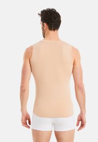 Nude tank top with a fitted design, sleeveless style, and smooth texture, paired with white briefs. View from the back.